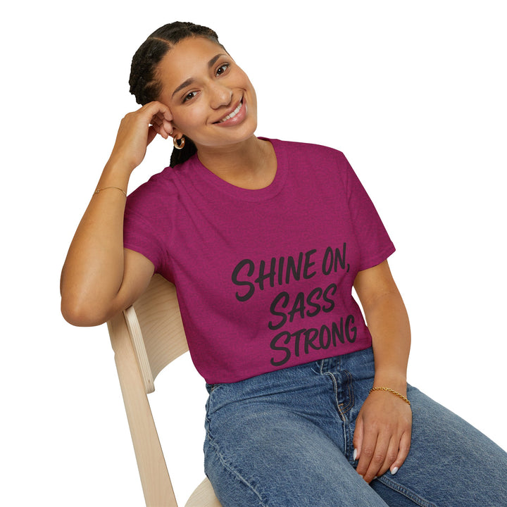 Female model  wearing a purple t-shirt with 'Shine on, Sass Strong' text, sitting on a chair.